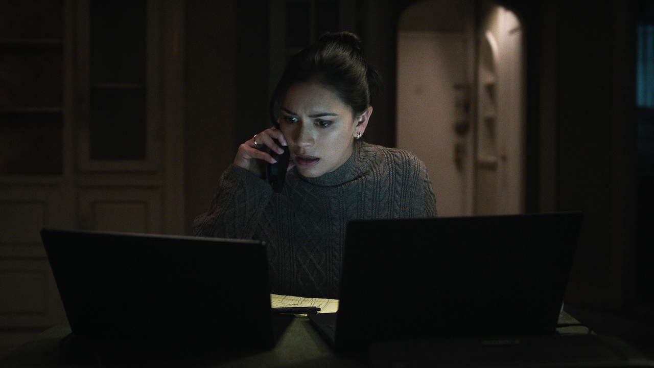 Rose Larkin seated in front of laptops and talking on cell phone in The Night Agent Season 2