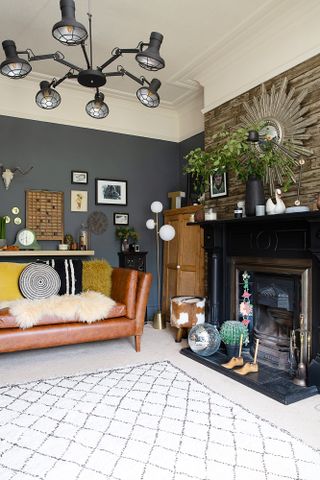 A living room with brown leather sofa, black and white rug, black Victorian-style fireplace and wallpapered brick-pattern feature wall