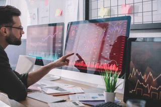 Side view of data analyst pointing with finger at charts on computer monitor while testing protection of computer systems
