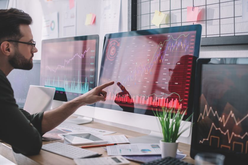 Side view of data analyst pointing with finger at charts on computer monitor while testing protection of computer systems