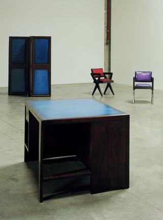 Furniture items in red, purple and blue stand in a concrete room