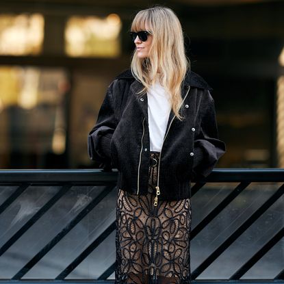 blonde fashion week attendee wearing sunglasses, leather jacket, white t-shirt, and sheer skirt