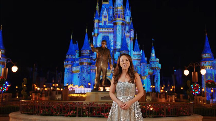 Lacey Chabert stands in front of the famous castle lit up at night and statue of Walt Disney at Disney World.
