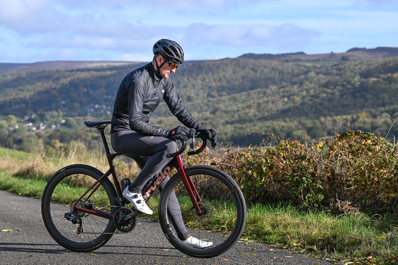 Male riding looking at his computer whilst sat on the top tube of his bike wearing a black Castelli Squall Shell