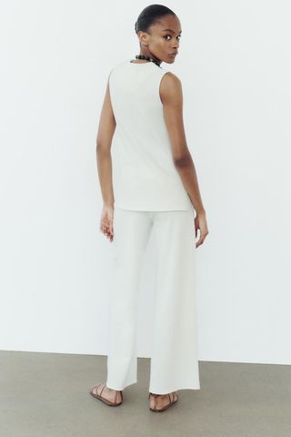 Soft sleeveless top and matching pants in white on model facing backwards. 