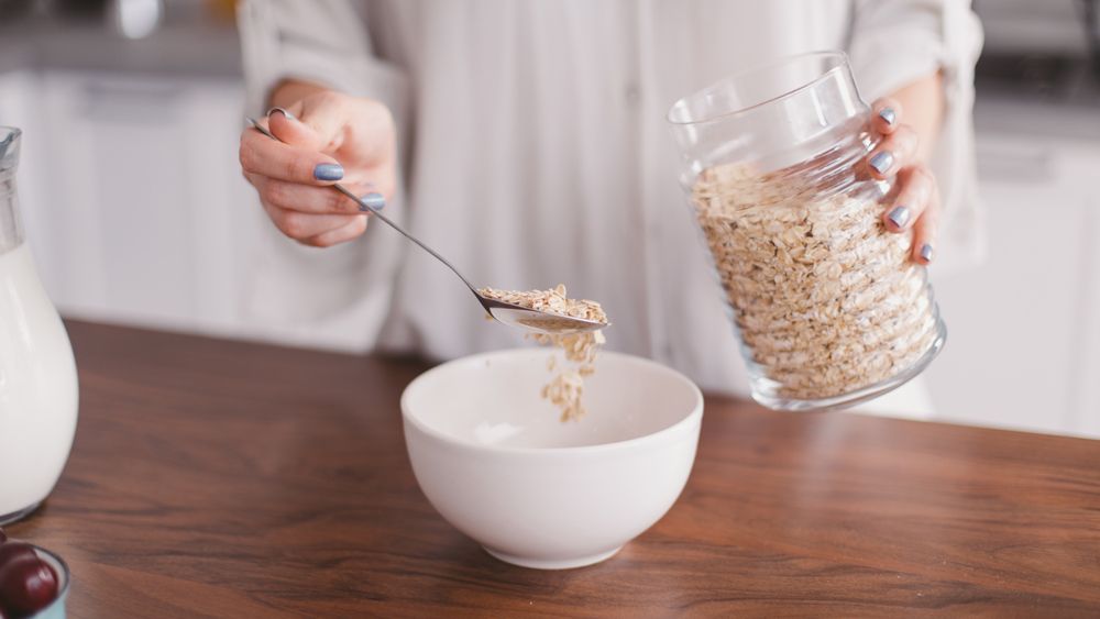 Close up of woman’s hands spooning oats into a bowl