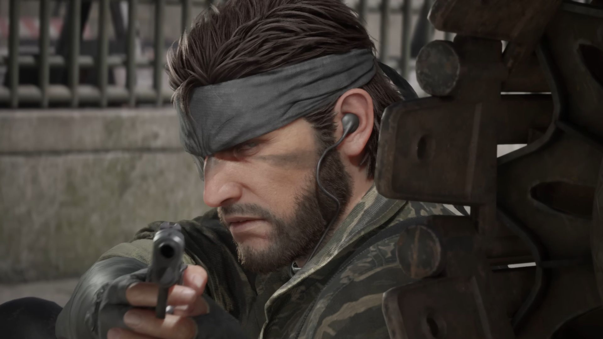 Snake from the Metal Gear Solid 3 remake. He&#039;s hiding behind some sort of metal cover and aiming a pistol at the camera.