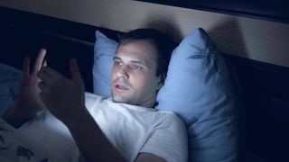 A man uses his smartphone in bed at night