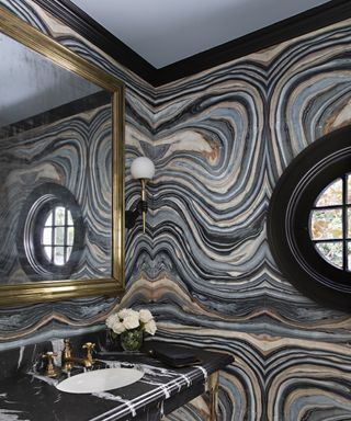 A powder room with full wall marble covering in striped shades of grey and black, with gold fittings