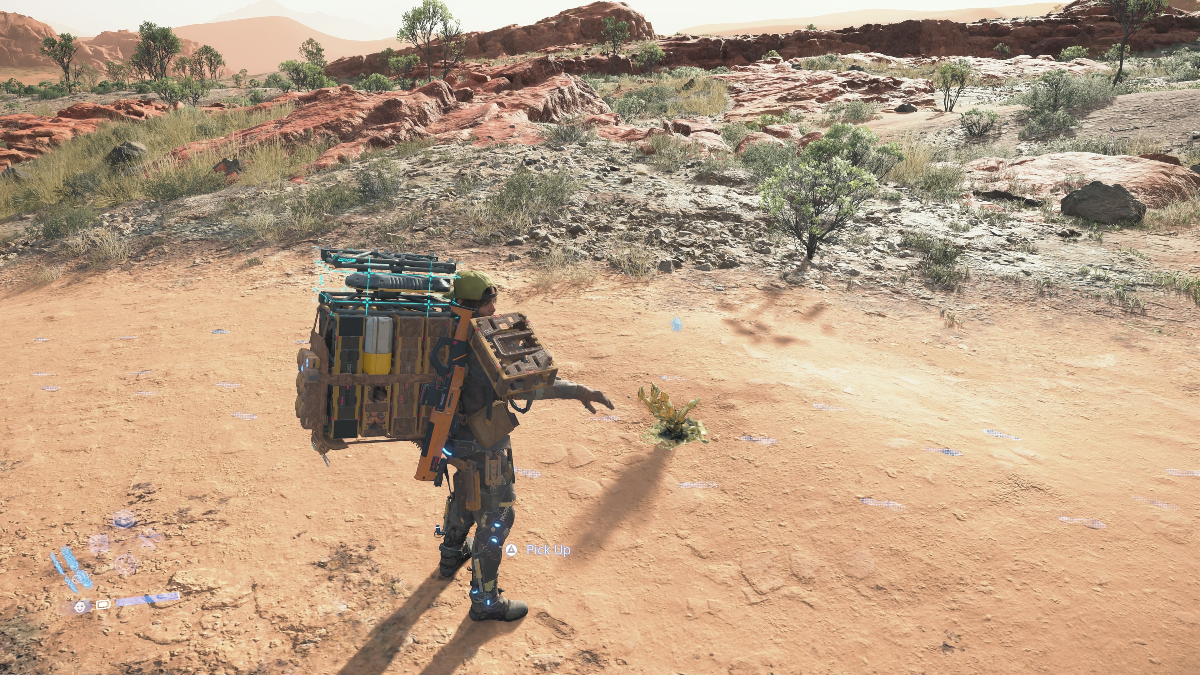 Death Stranding 2 carry capacity: Sam standing in a desert looking at his arm while wearing an exosuit.