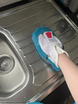 A steam cleaning mitt being used to sanitize a sink draining board