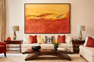 A neutral living room with red and orange wall art