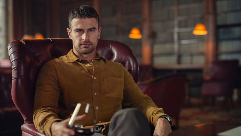 Eddie Horniman (Theo James) sits in a red armchair, with a glass of red wine in hand in Netflix&#039;s &quot;The Gentlemen&quot;