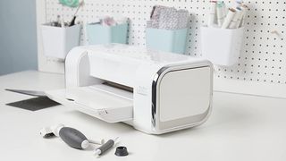 The best embossing machine, a white embossing machine is on a white table surrounded by craft card, tools and materials