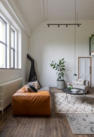 A living room with unpolished wooden flooring and terracotta slubby leather sofa with indoor houseplant in background