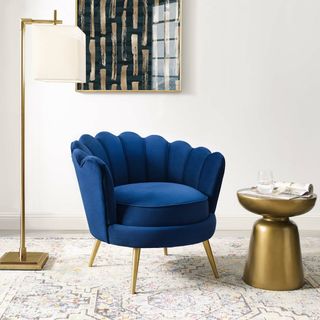 Mercer 41 Demers Barrel Chair in a stylish living room with a white rug, gold side table and gold lamp, and artwork on the walls