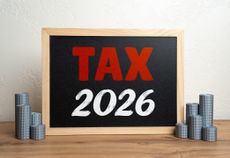 Tax 2026 on a small chalkboard flanked by stacks of silver coins