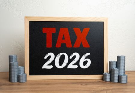 Tax 2026 on a small chalkboard flanked by stacks of silver coins