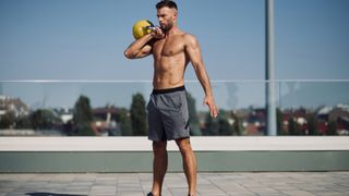 Man outdoors holding kettlebell on shoulder in racked position during clean and jerk exercise