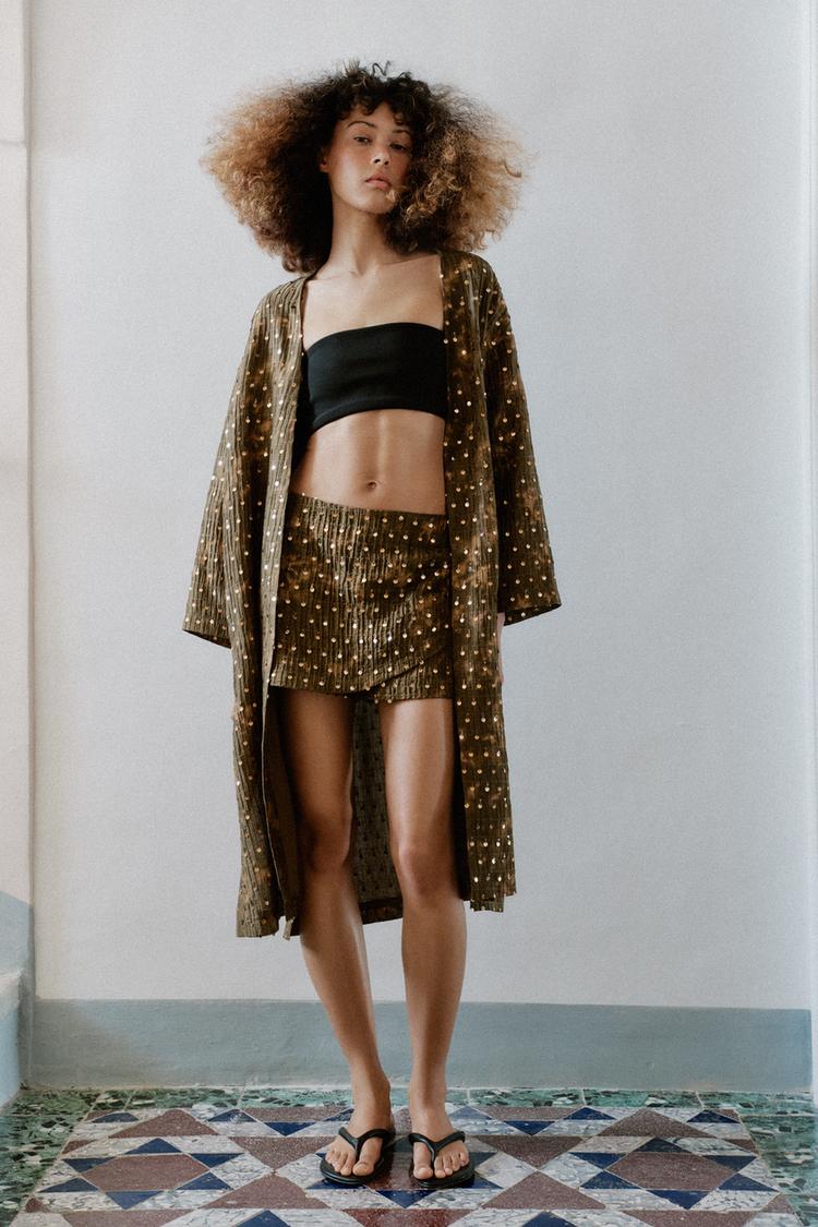 Woman wears brown kimono and mini skirt with black bandeau and sandals.