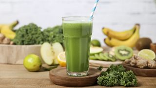 a green smoothie with fruit and veg on a board around it