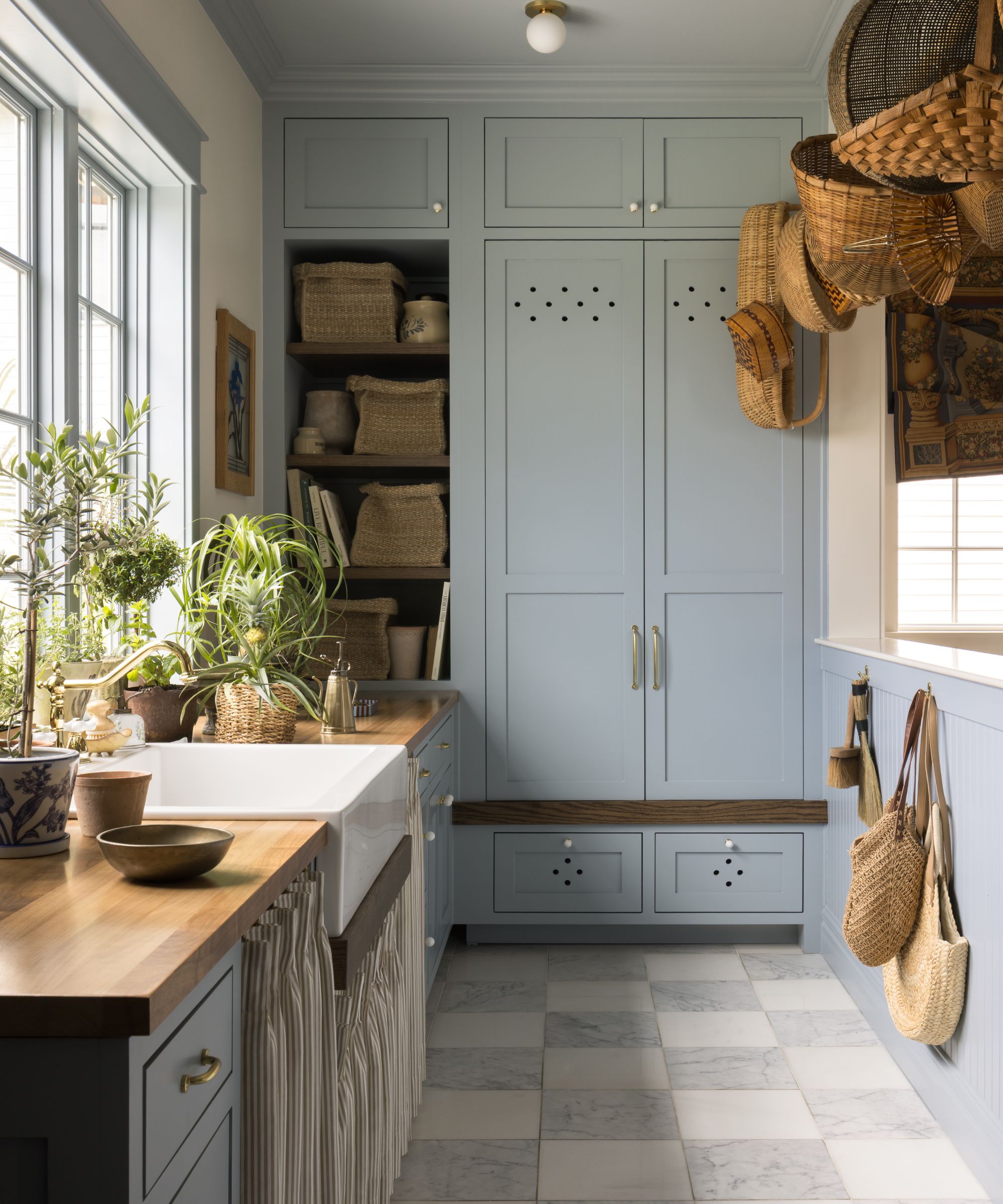 a large light blue painted mudroom slash garden room with tall cabinetry, butlers sink, skirted storage and checkboard floor tiles