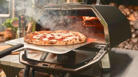 Ooni Karu 2 Pro with a fresh pizza being taken out of it on a metal pizza peel. 