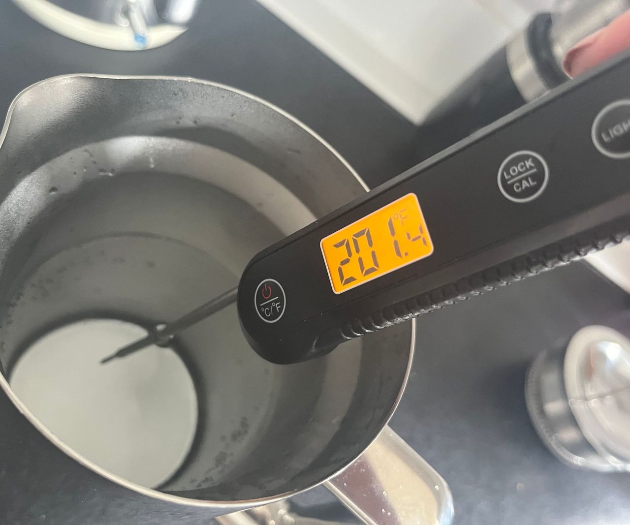 a digital thermometer reading the temperature of water in a stainless steel coffee press. It shows 201F