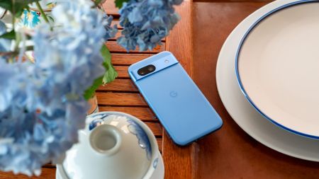 The blue Google Pixel 8a on a tea tray with blue hydrangeas above it