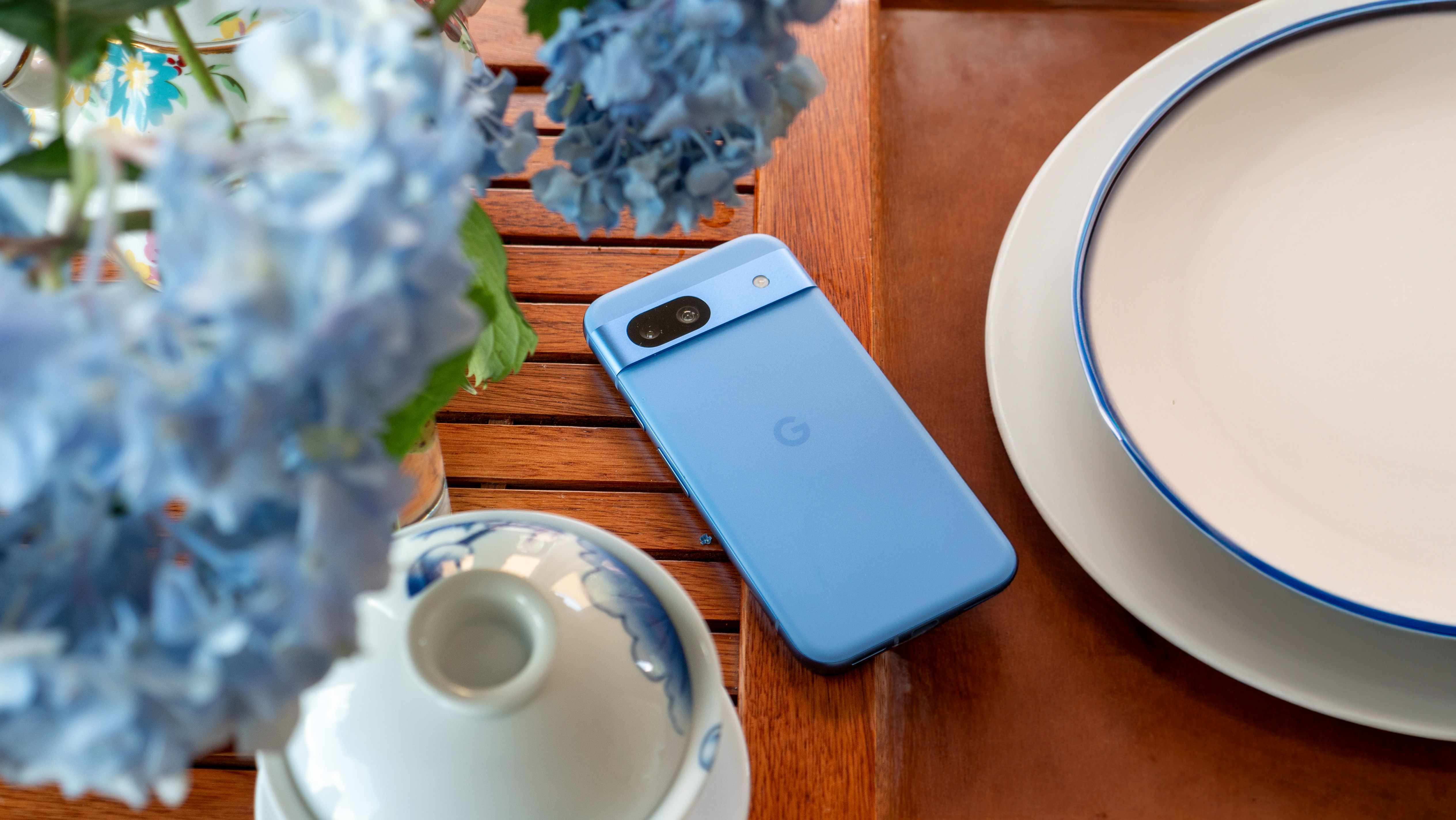 The blue Google Pixel 8a on a tea tray with blue hydrangeas above