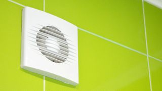 White bathroom extractor fan high on line green wall tiles near ceiling