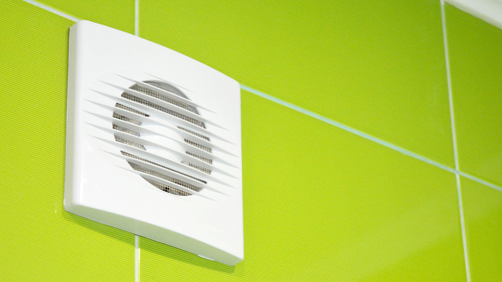 White bathroom extractor fan high on line green wall tiles near ceiling
