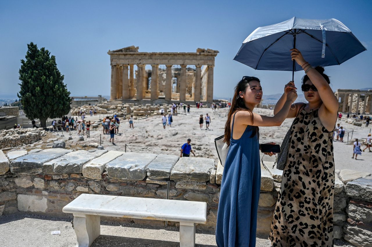 Women stand under an umbrella to beat the heat at the Acropolis in Athens