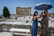 Women stand under an umbrella to beat the heat at the Acropolis in Athens