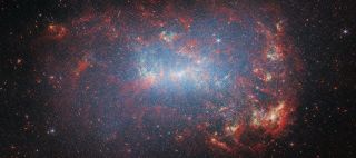 A sparkly galaxy is seen against the darkness of space. There are red crevices and blueish lights.
