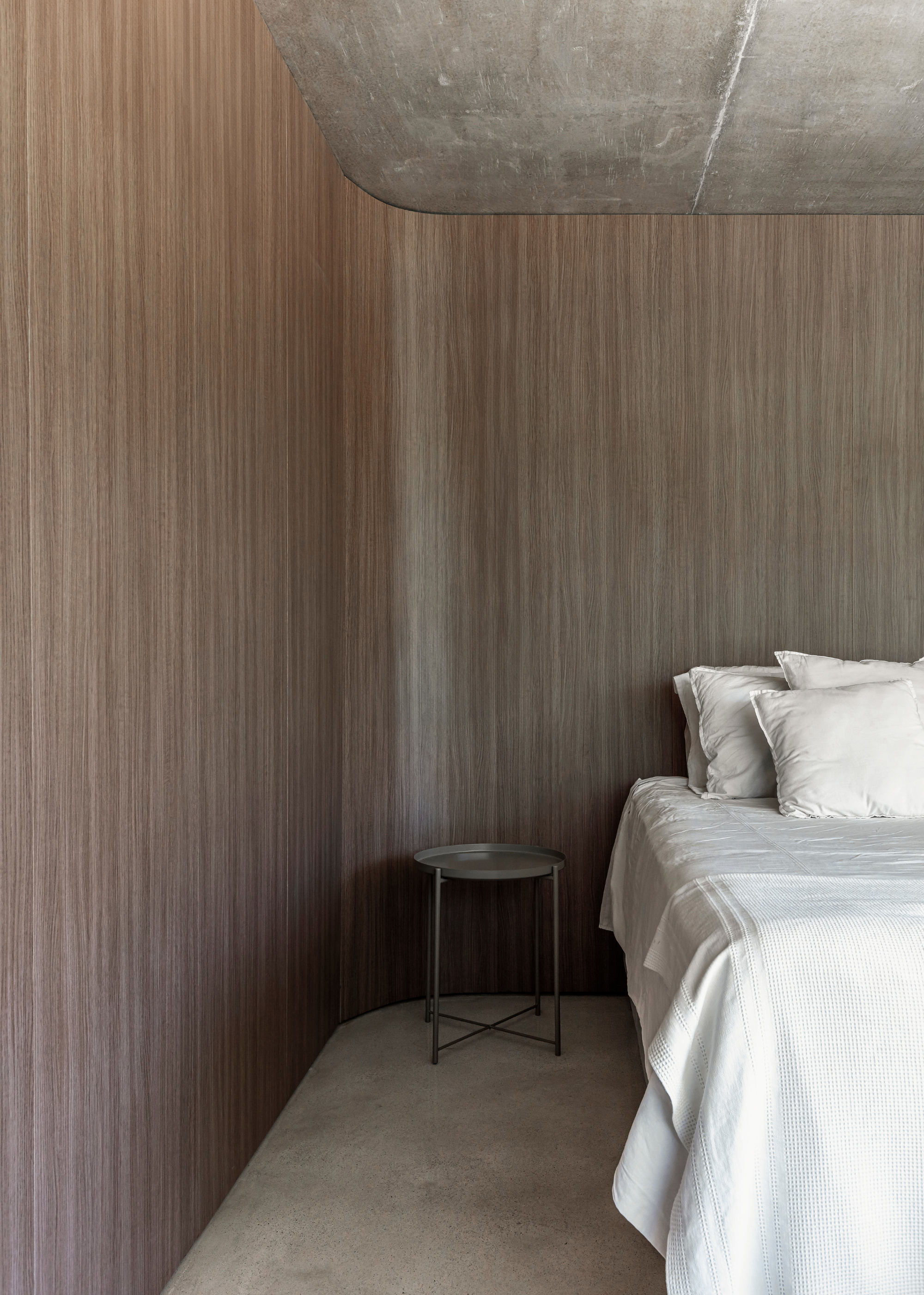 A minimalist bedroom with a metal stool and curved wood panel walls