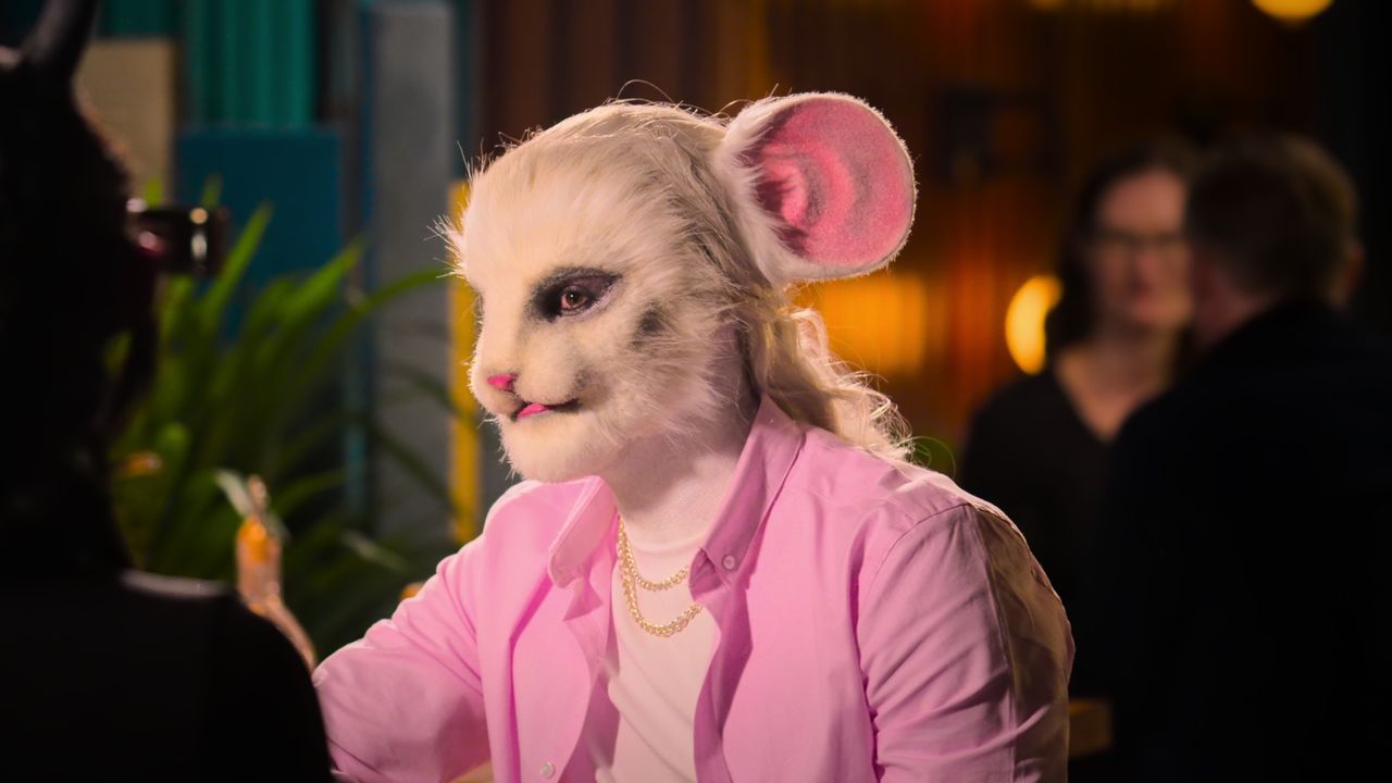 A film still from Sexy Beasts Netflix dating show which depicts the &#039;mouse&#039; in a bright pink jacket sitting at a bar