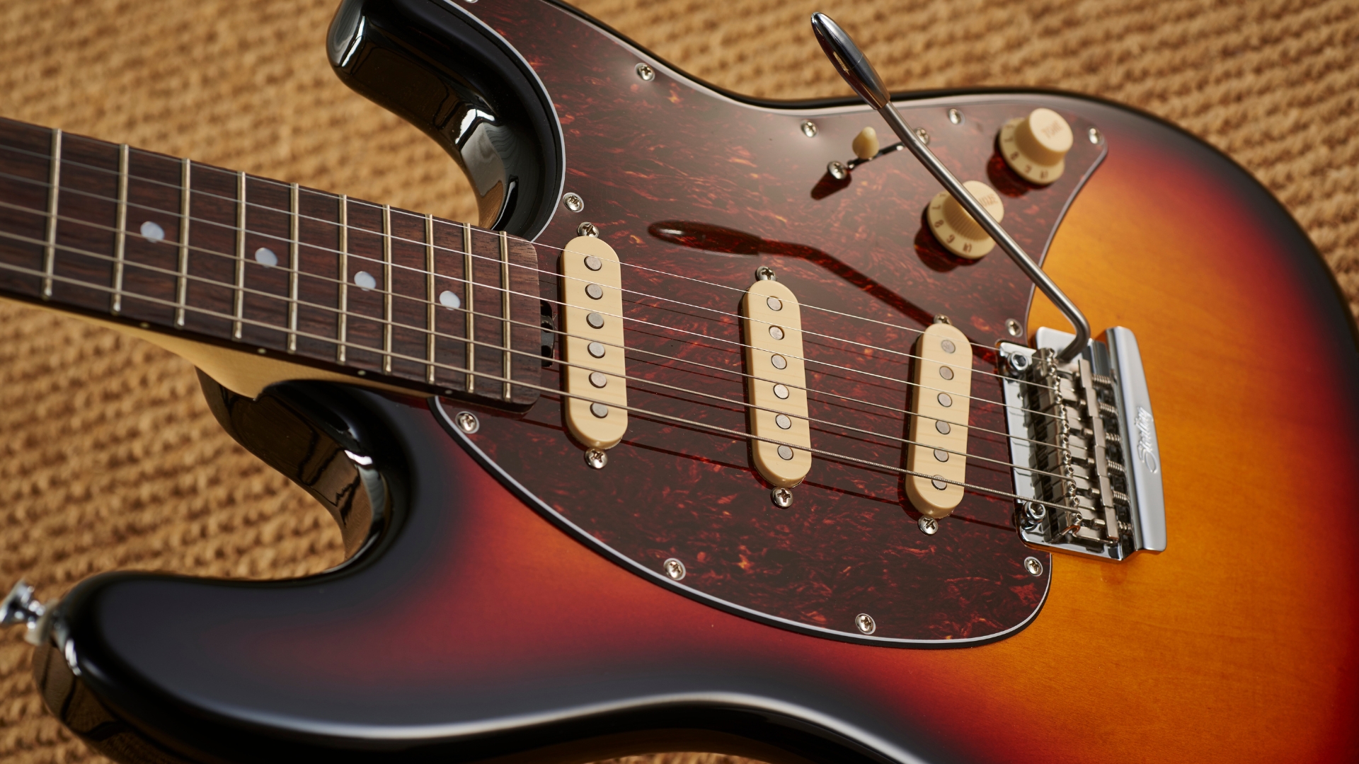 A Sterling by Music Man electric guitar on a rug