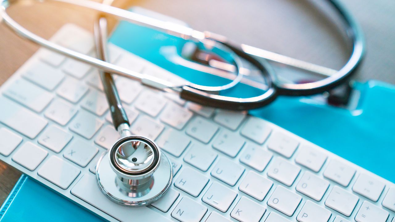 A stethoscope lies on top of a medical chart and a computer keyboard.