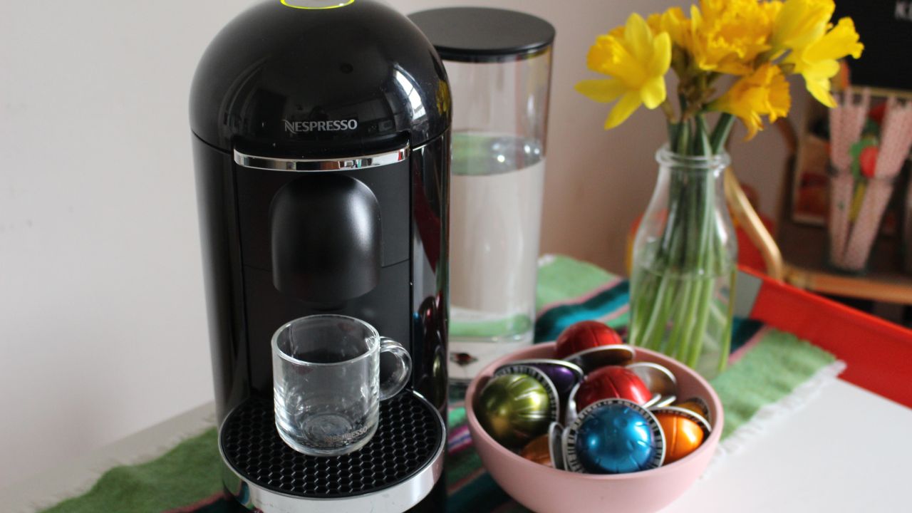 Nespresso Vertuo Plus coffee maker on kitchen counter with a bowl of colorful coffee capsules