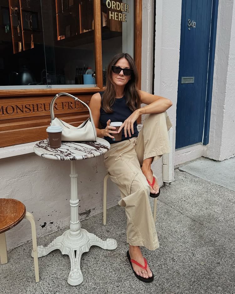 @kimturkington_ wears a pair of sand-coloured trousers with red sandals and a black top