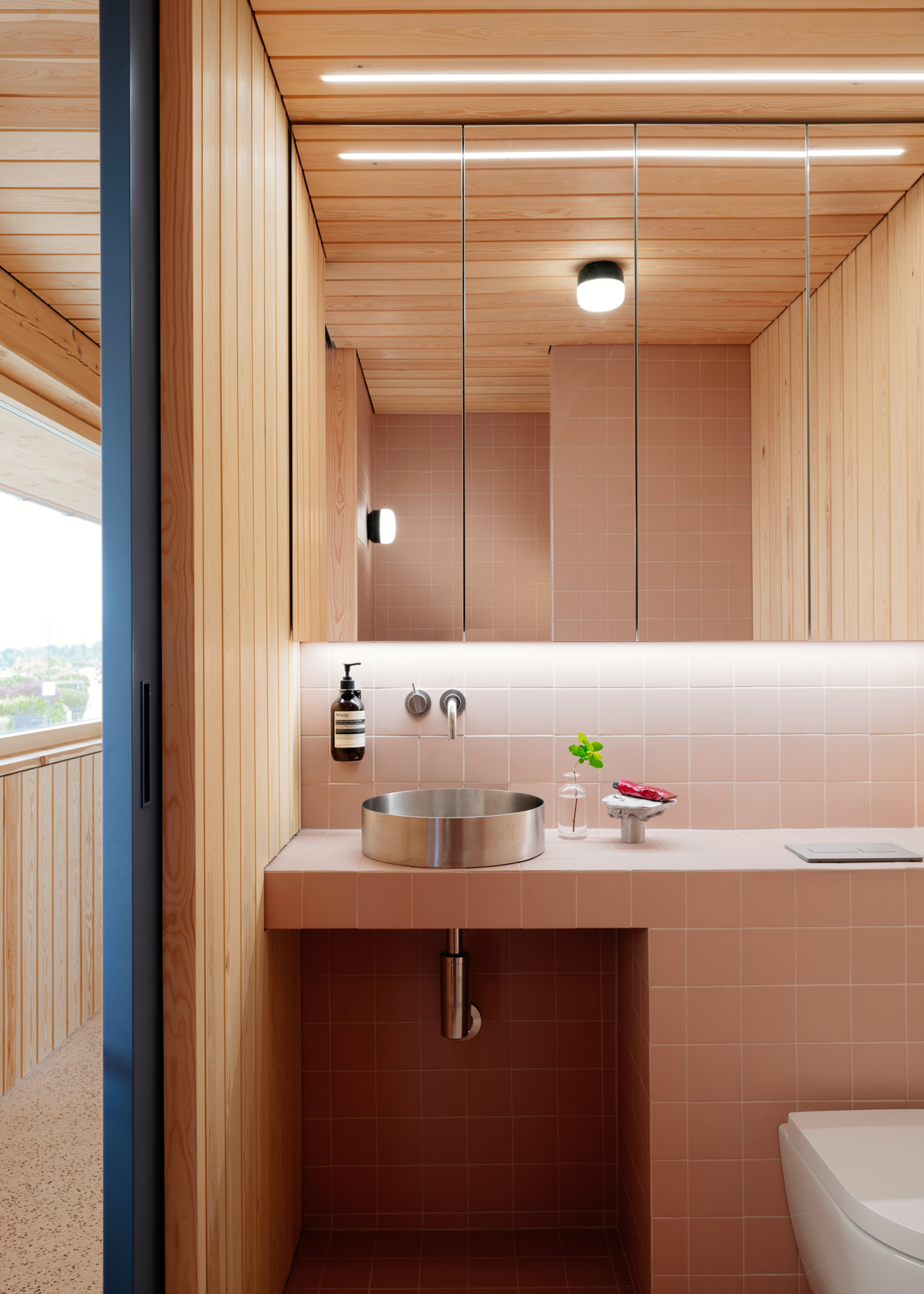 A bathroom with pink square tiles, wood panelled walls, and a steel sink