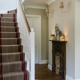 A hallway with a staircase and a fireplace displaying some burning tea lights and wall lights above it