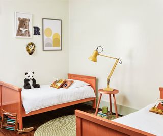 two single beds painted orange with cream walls, bear poster and yellow anglepoise style lamp on stool