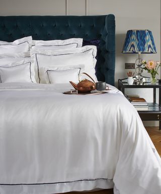 A bedroom with white Mulberry silk bedding and Chesterfield-style teal velvet headboard decor