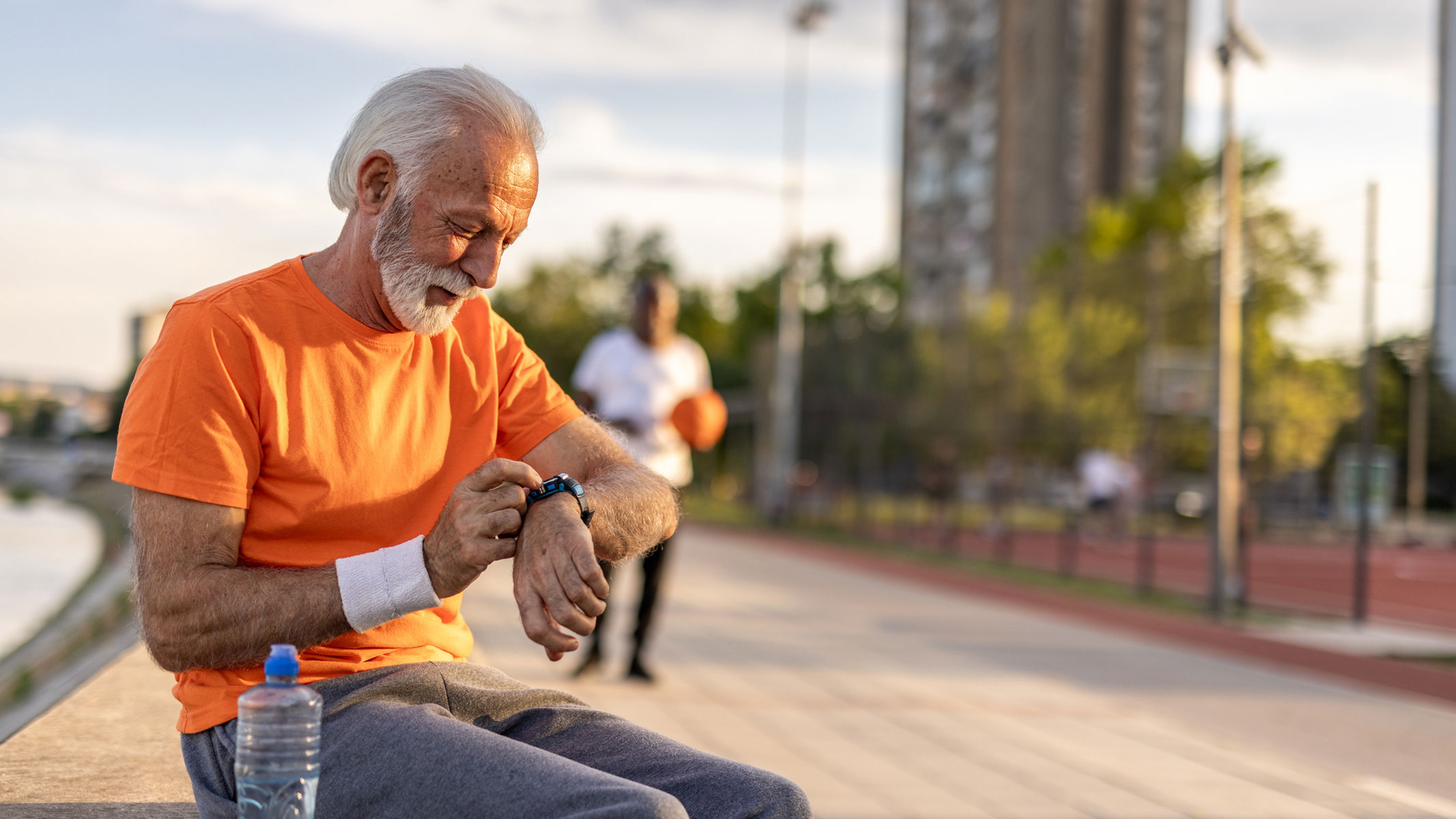 A picture of an elderly man checking his smartwatch while resting on a bench outside