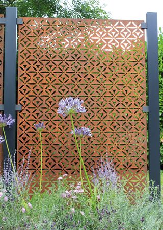 A weathered steel panel fence with flowers in front of it