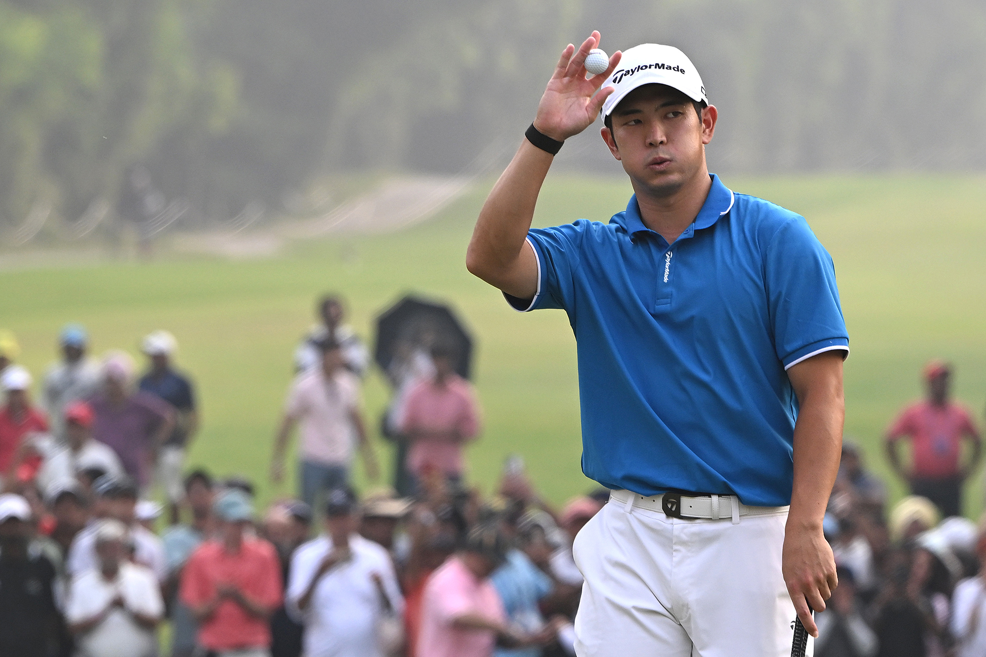 Keita Nakajima raising the golf ball to the crowd in thanks after holing a putt
