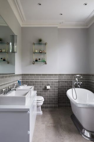 grey bathroom with half a wall of grey metro tiles, freestanding bath bath and double sink