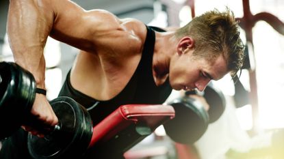 best dumbbells: Shot of a muscular young man working out on a weight bench with dumbbells